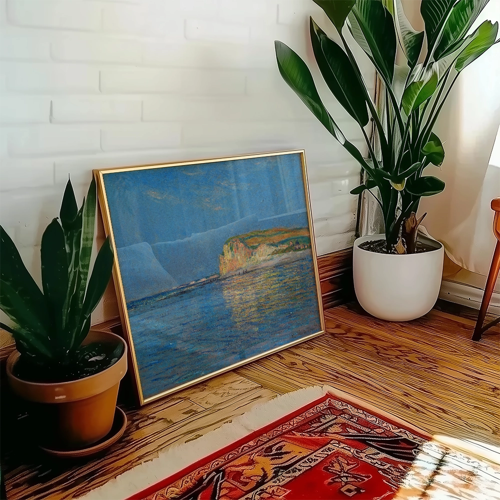 Framed painting of a coastal landscape with blue water and a rocky shore, set against a bright background, displayed near a potted plant in a cozy indoor setting.