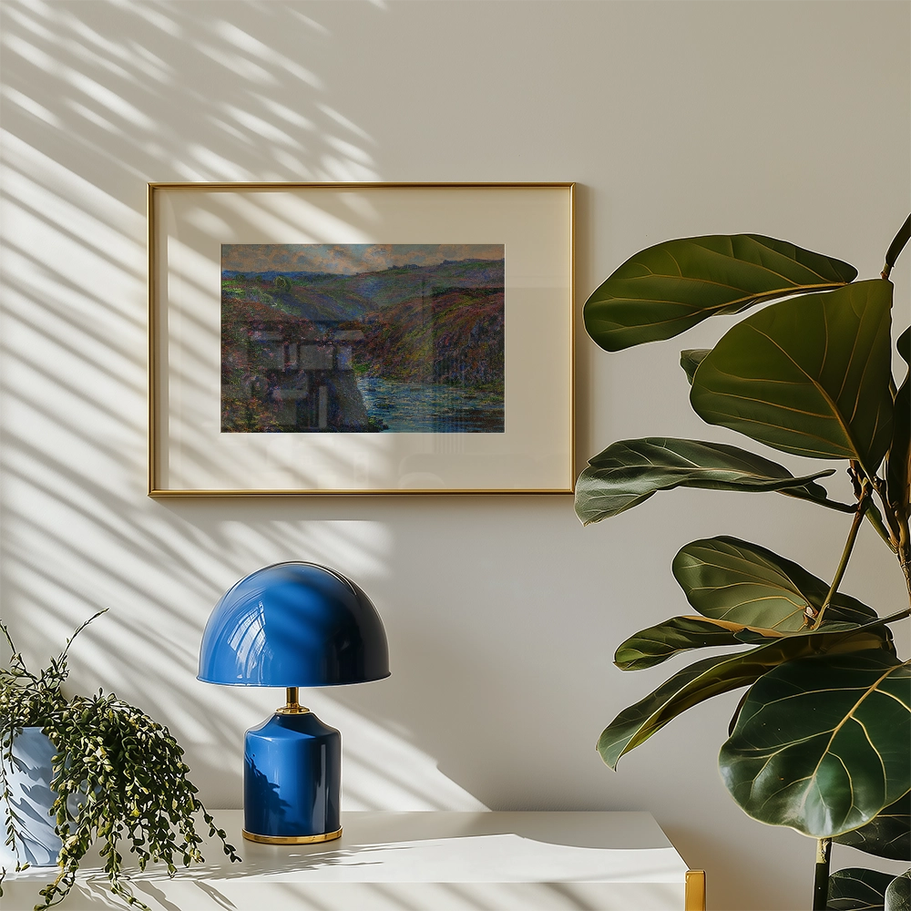Framed painting of a landscape in shades of blue and green, displayed on a wall next to a blue lamp and a leafy plant.