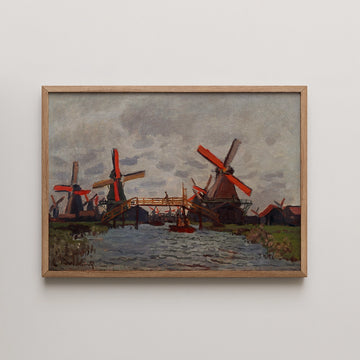Painting of windmills with red blades beside a river, framed in wood.