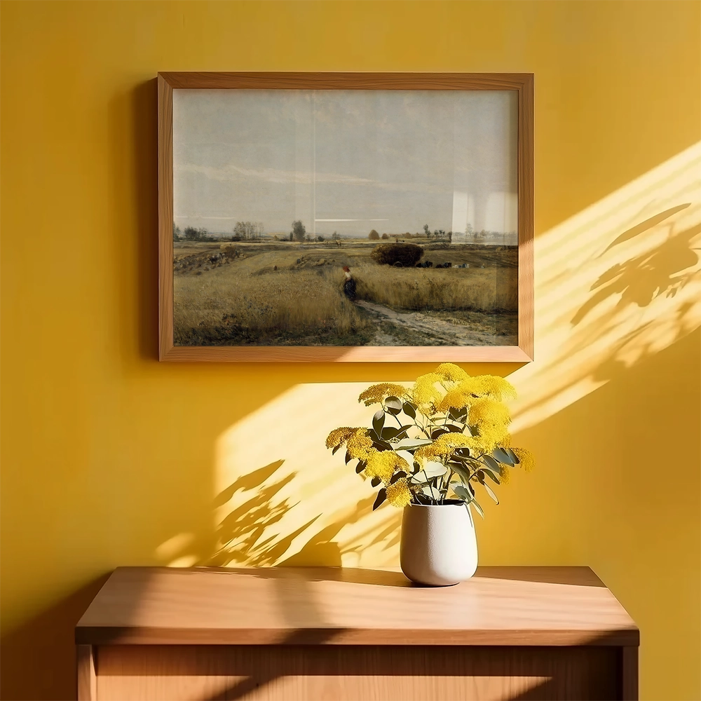 Framed landscape painting of a grassy field under a cloudy sky, displayed on a yellow wall with a vase of yellow flowers on a wooden table below.