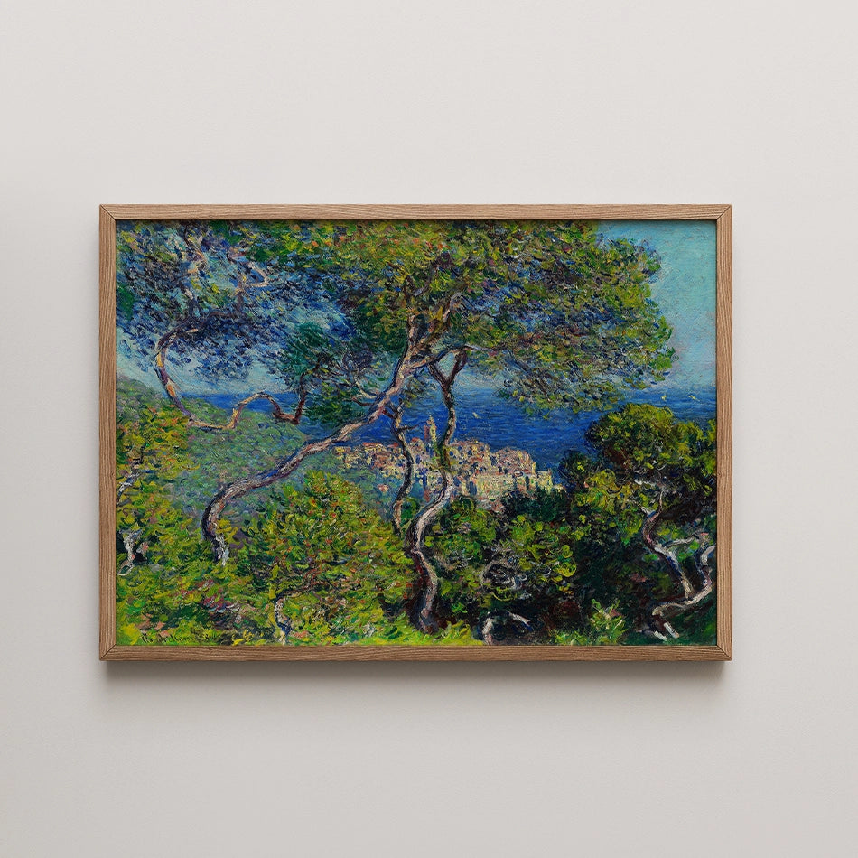 Painting of a lush landscape featuring green trees and a blue sea in the background, framed in a light wooden frame.