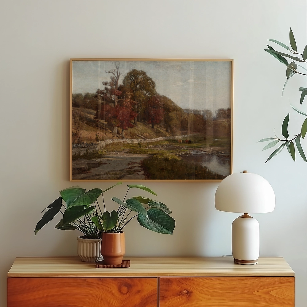 Framed landscape painting of rolling hills and trees in autumn colors displayed above a wooden console with plants and a lamp.