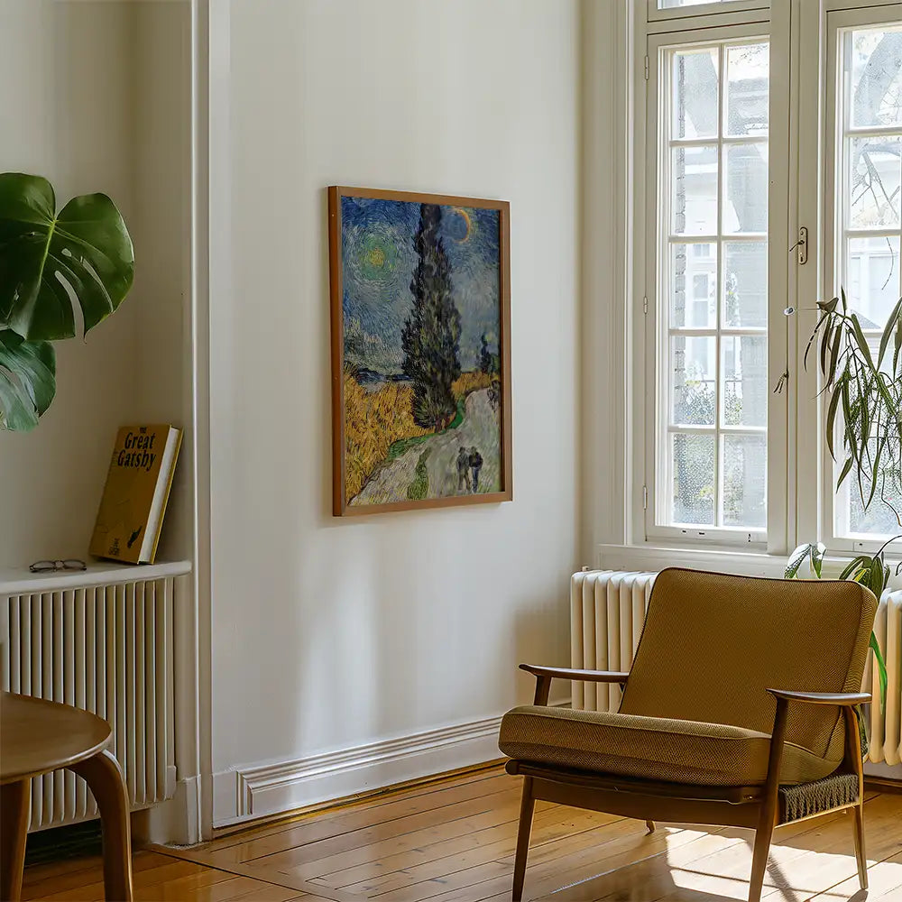 Framed landscape painting of a tree-lined path on a wall in a modern living room with a mid-century armchair and a potted plant.