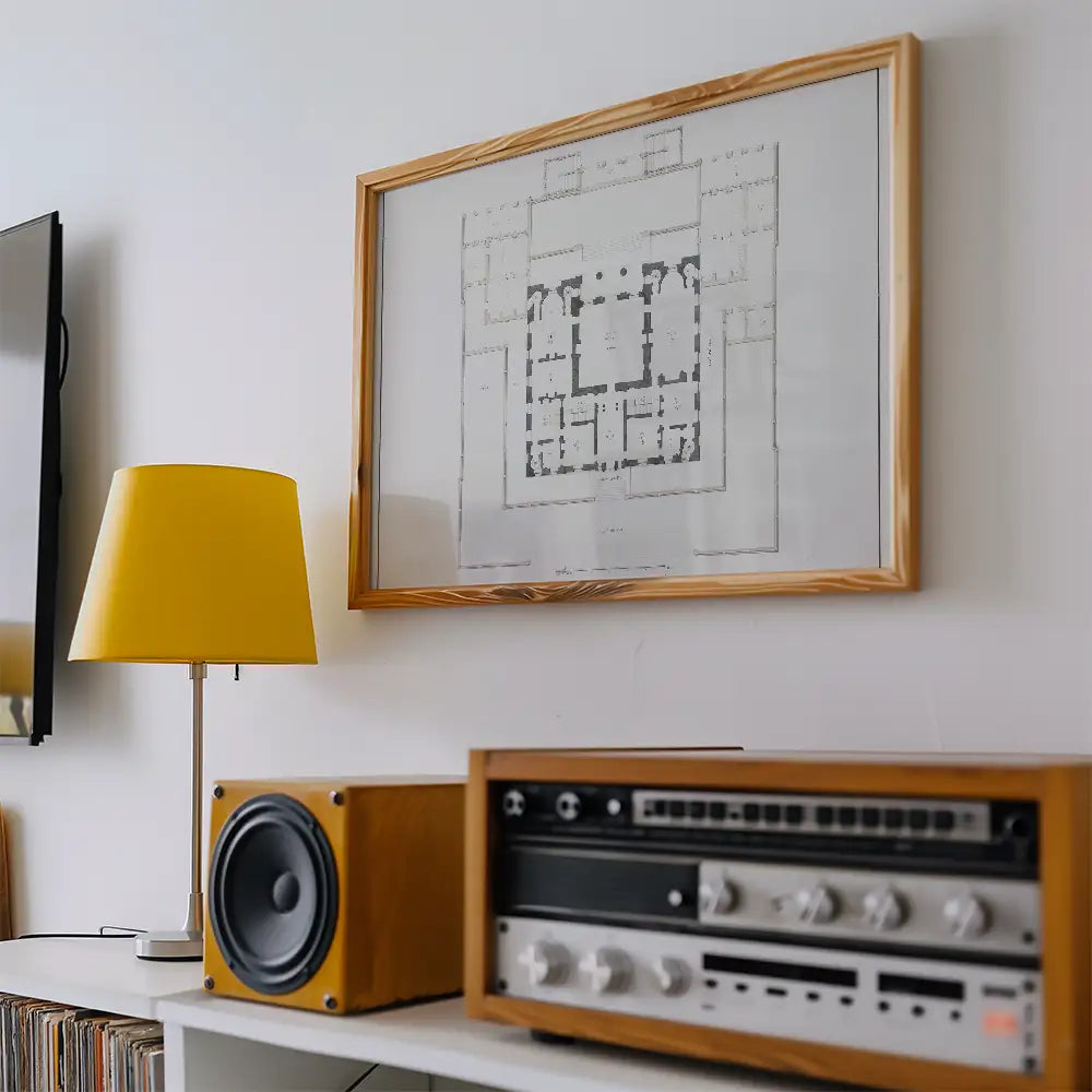 Framed architectural blueprint art print on a wall with a yellow lamp and vintage audio equipment in a styled room setting.