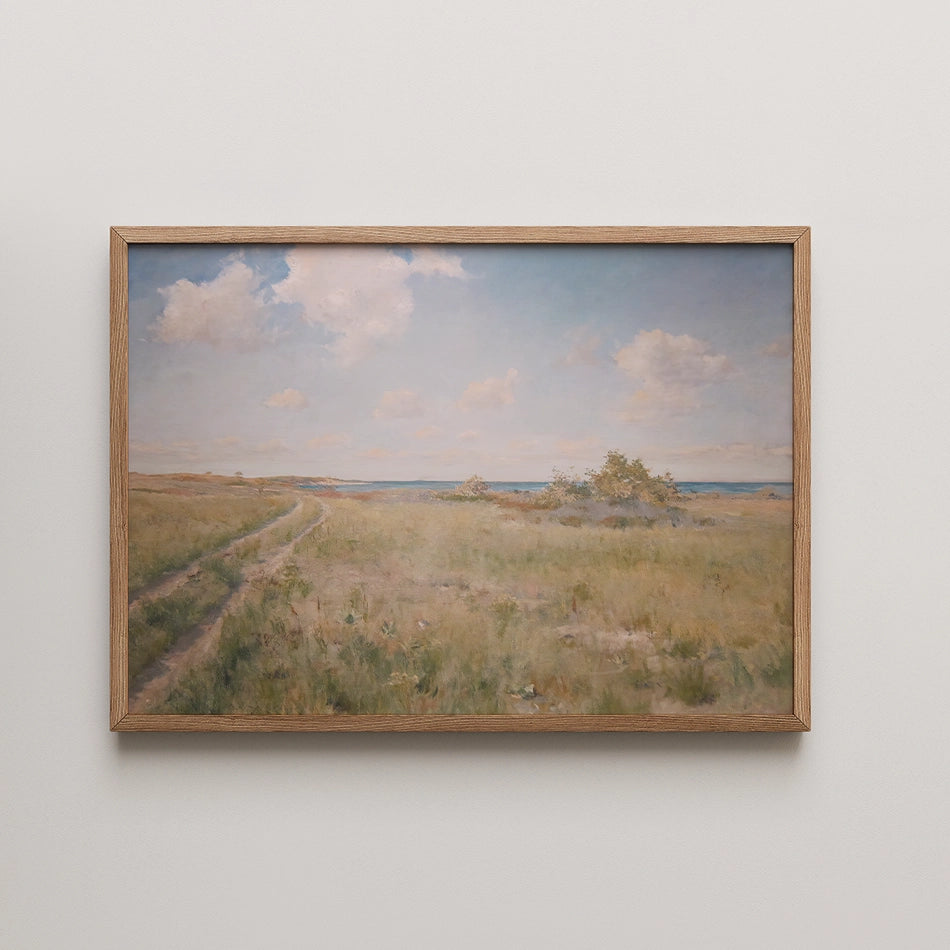 Landscape painting featuring a serene field with a dirt path leading towards a distant body of water under a blue sky with fluffy clouds, framed in light wood.