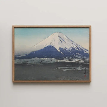 Mountain landscape painting featuring a snow-capped peak and blue sky, framed in natural wood.