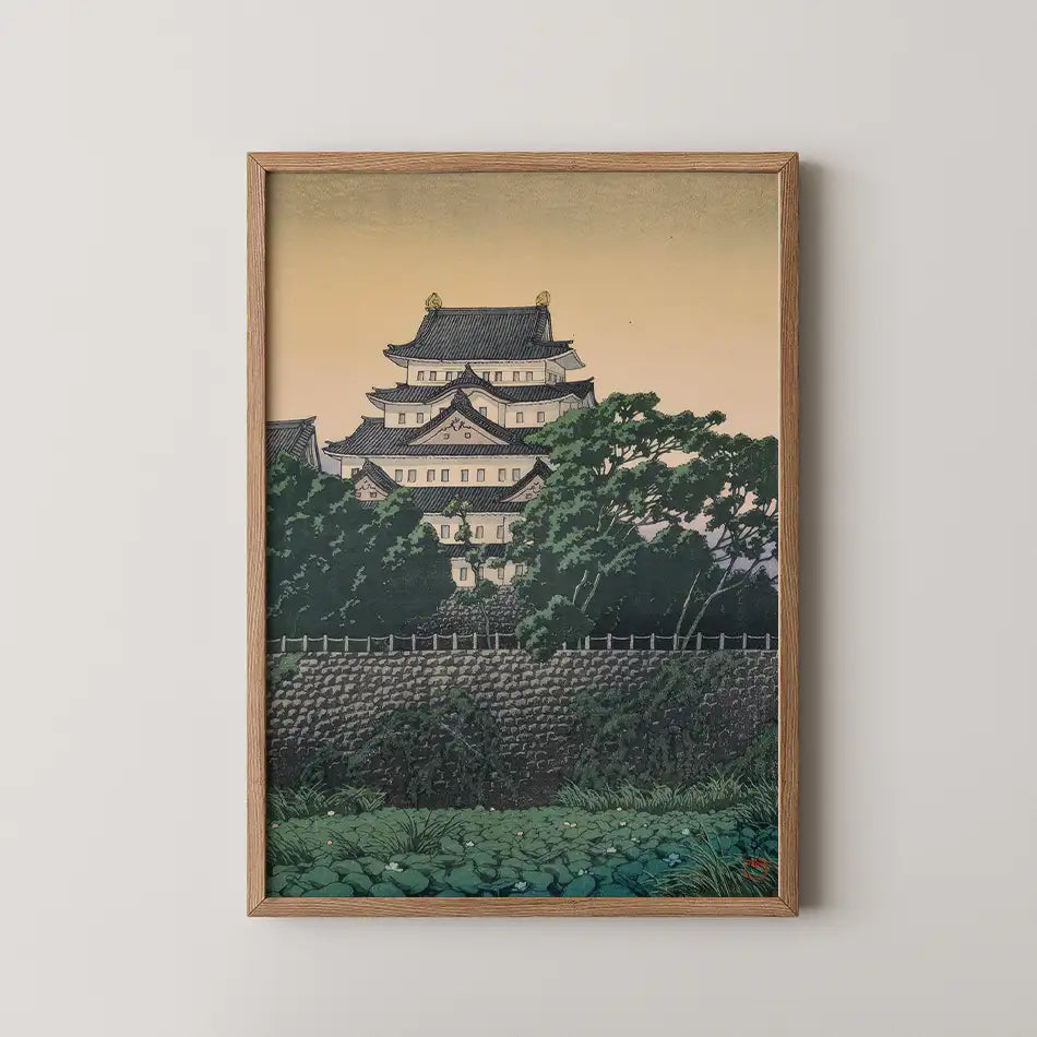 Framed painting of a traditional Japanese castle surrounded by lush greenery and a serene sunset sky.