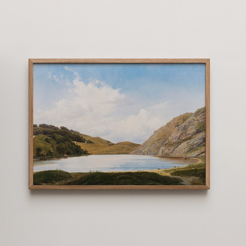 Landscape painting of a serene lake surrounded by hills and trees, framed in wood.