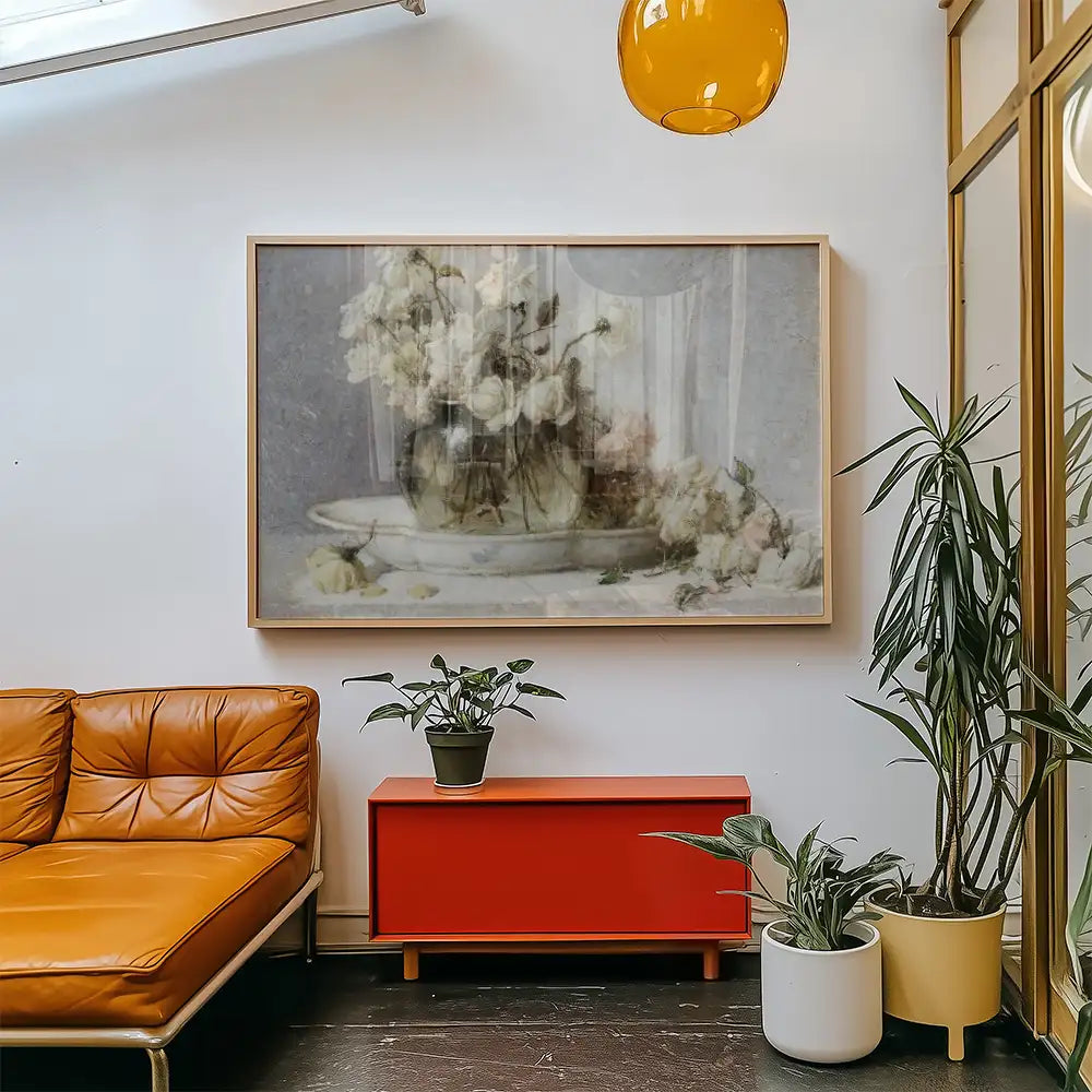 A serene floral painting in a light wooden frame, displayed on a white wall above a modern orange couch and a red side table with potted plants.