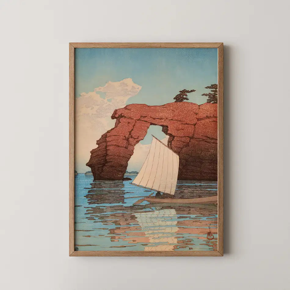 Framed painting of a sailboat passing through a rock arch, with reflections on the water and a serene sky.