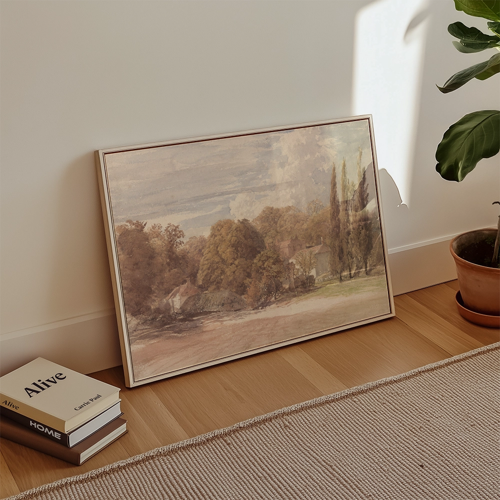 A framed landscape painting leaning against a wall, with a potted plant and books in the foreground.