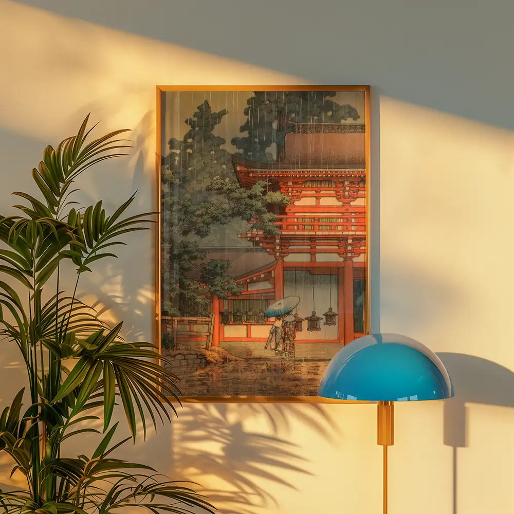 Traditional Asian landscape painting featuring a red-roofed structure and a figure with an umbrella, framed on a wall beside a potted plant and a modern blue lamp.