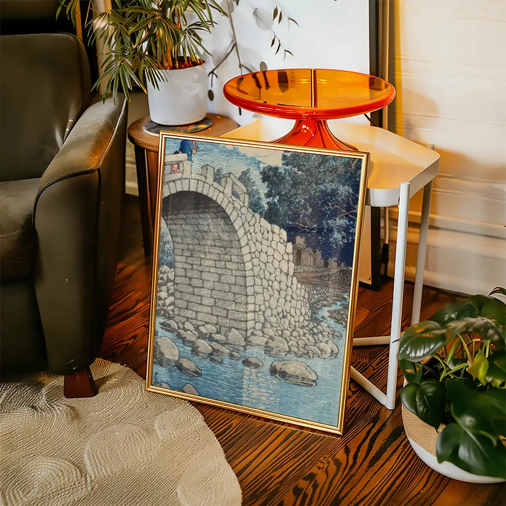 Framed painting of a stone bridge over a river, displayed in a cozy living room setting.
