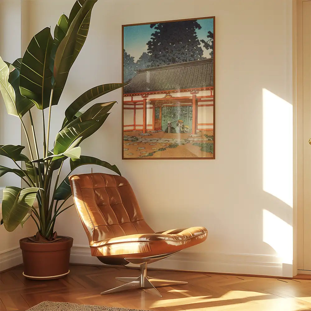 Painting of a serene garden scene framed on a wall next to a large green plant and a stylish brown chair in a sunlit room.