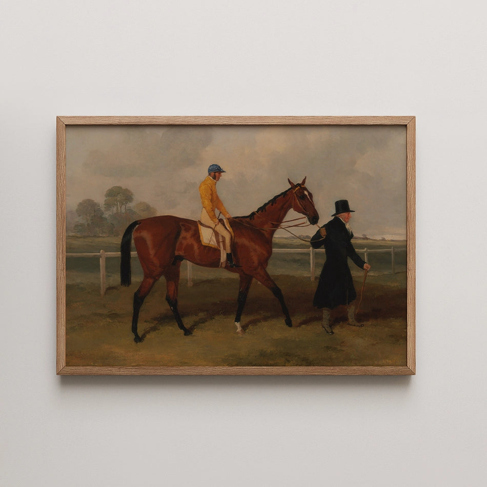 Painting of a horse with a jockey in yellow and a man in a black coat walking next to it, framed in wood.