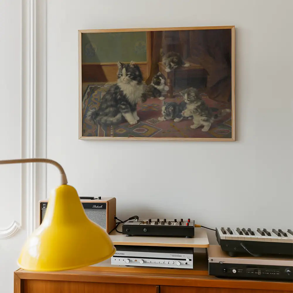 Framed painting of a mother cat with her kittens on a colorful rug, displayed on a wall above a wooden cabinet with a yellow lamp and vintage audio equipment.