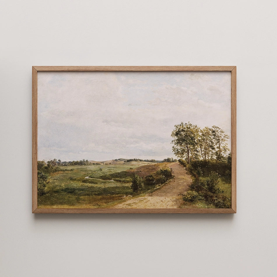 Framed landscape painting featuring a dirt path winding through green fields and trees under a cloudy sky.