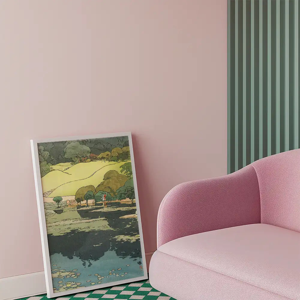Framed painting of a serene landscape featuring trees and a reflective pond, propped against a pink wall next to a pink sofa.