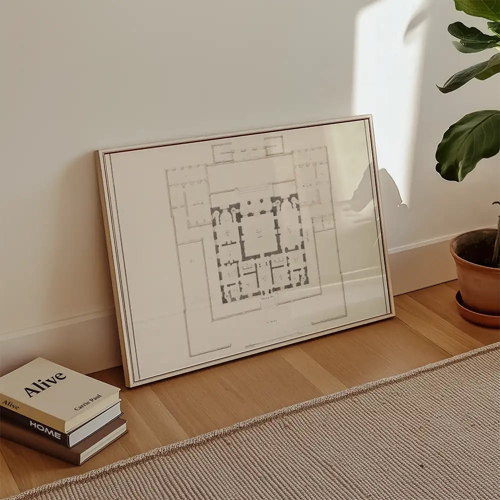 Framed architectural blueprint art piece leaning against a wall with a plant and books nearby.