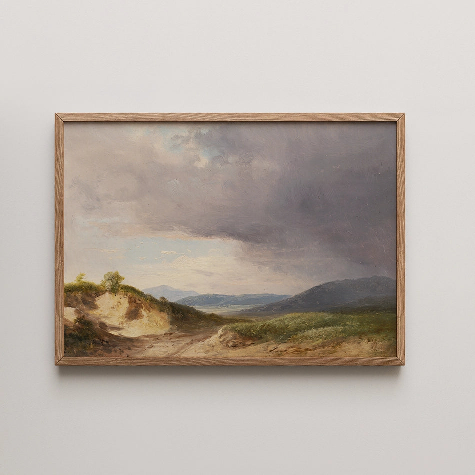 Landscape painting in a wooden frame depicting a natural scene with rolling hills, a sandy path, and a cloudy sky.