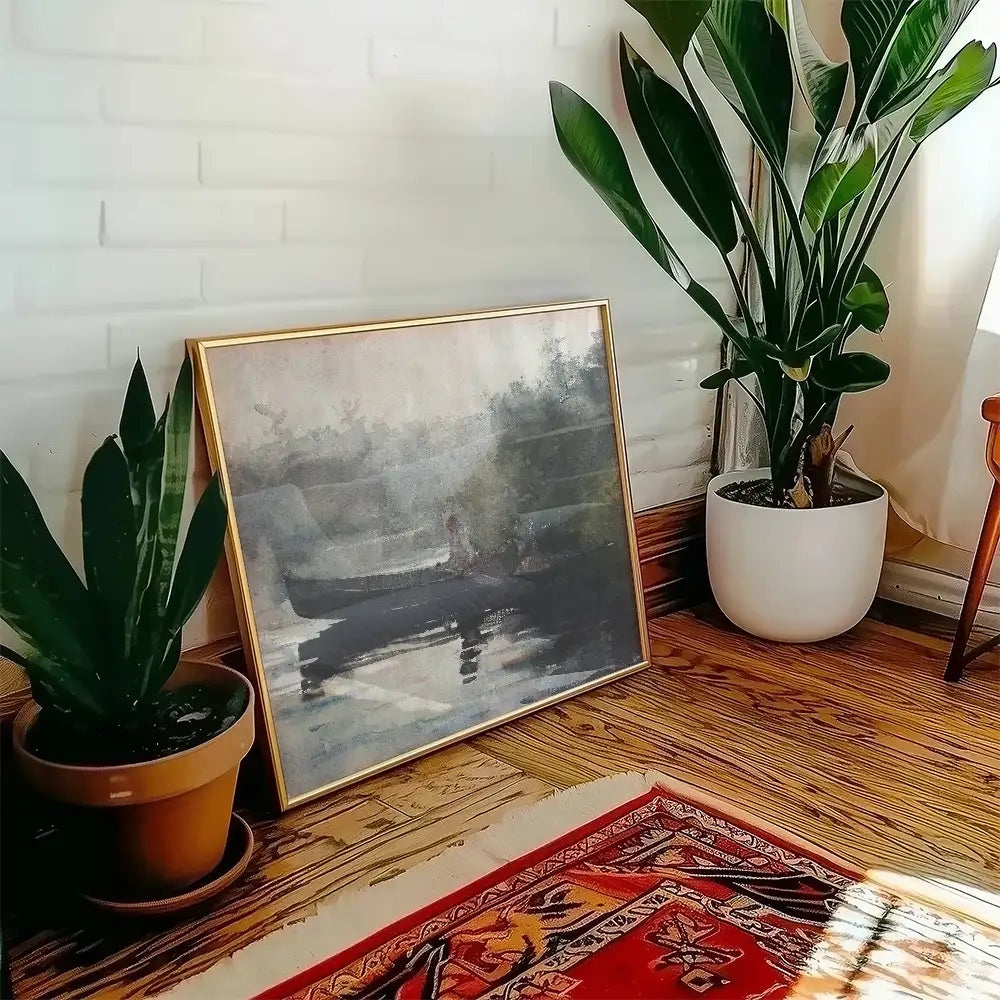 Framed painting of a serene landscape featuring a boat on water, placed beside potted plants in a cozy interior setting.