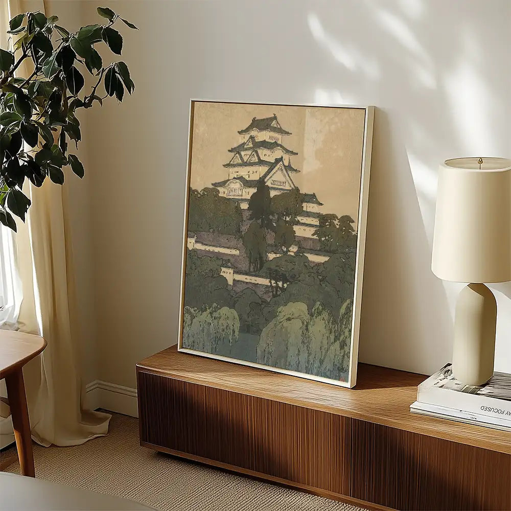 Framed painting of a traditional Japanese castle surrounded by greenery, displayed on a wooden console table with a lamp and decorative items.