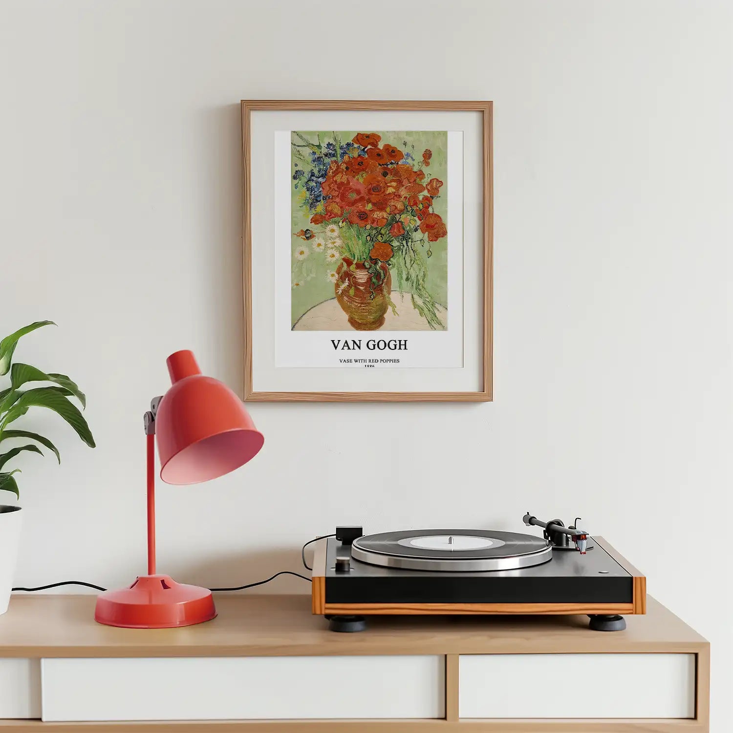 Framed Vincent van Gogh painting titled "Vase with Red Poppies" displayed on a wall above a modern record player and a red desk lamp with a potted plant nearby.