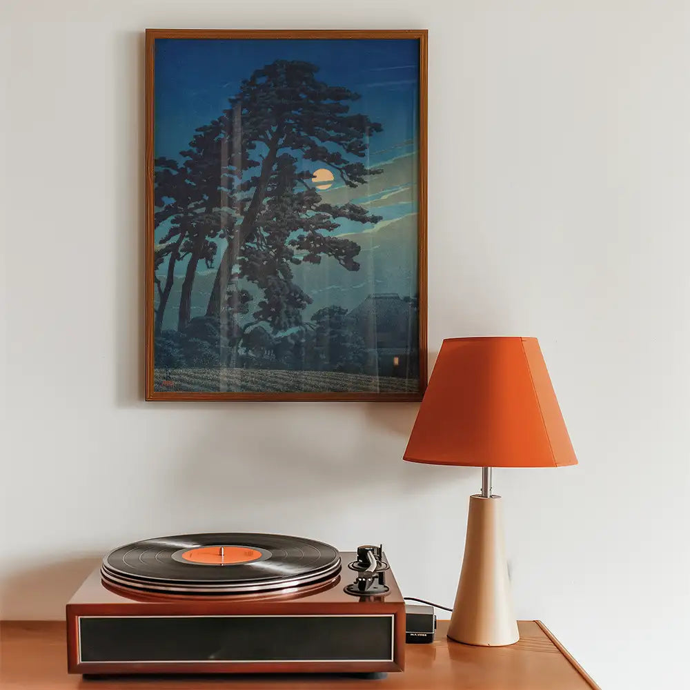 Framed painting of trees under a moonlit sky displayed above a vintage turntable and an orange table lamp.
