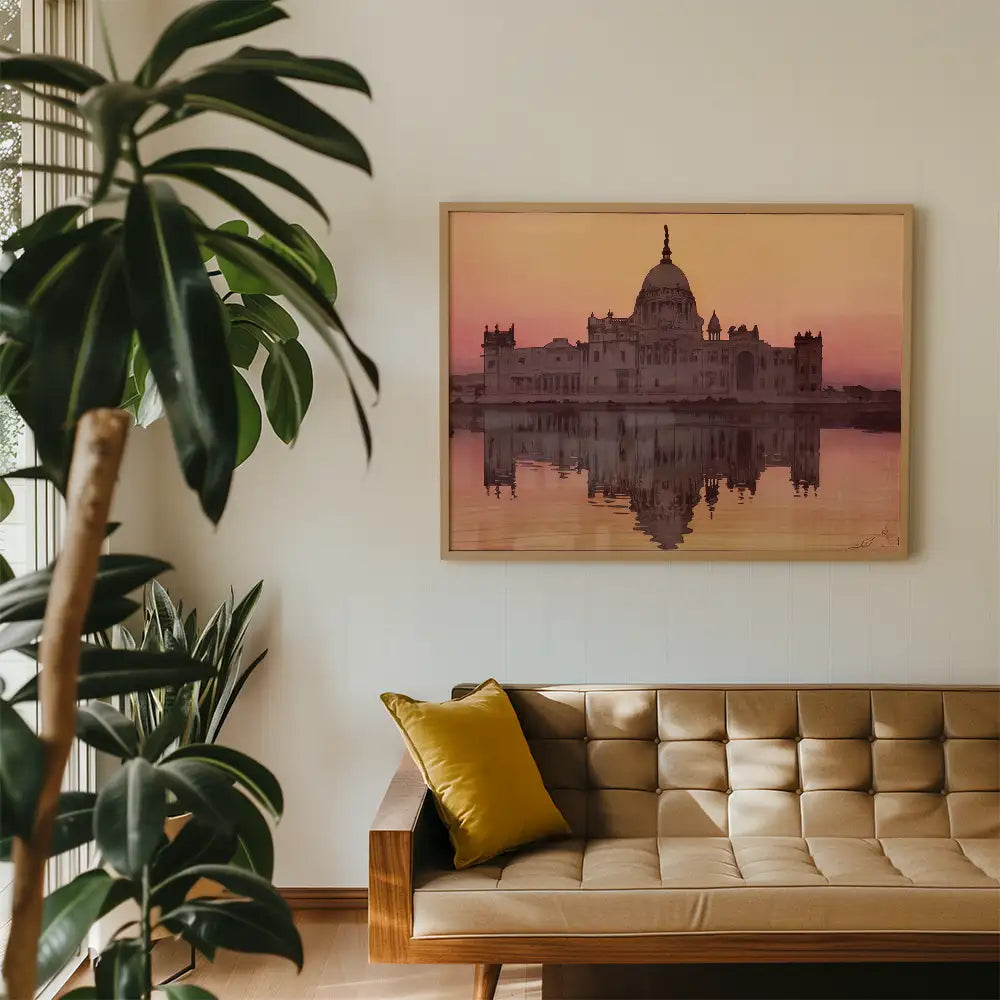 Framed painting of a palatial building reflected in water, displayed on a wall above a modern couch with a yellow pillow in a cozy interior space.