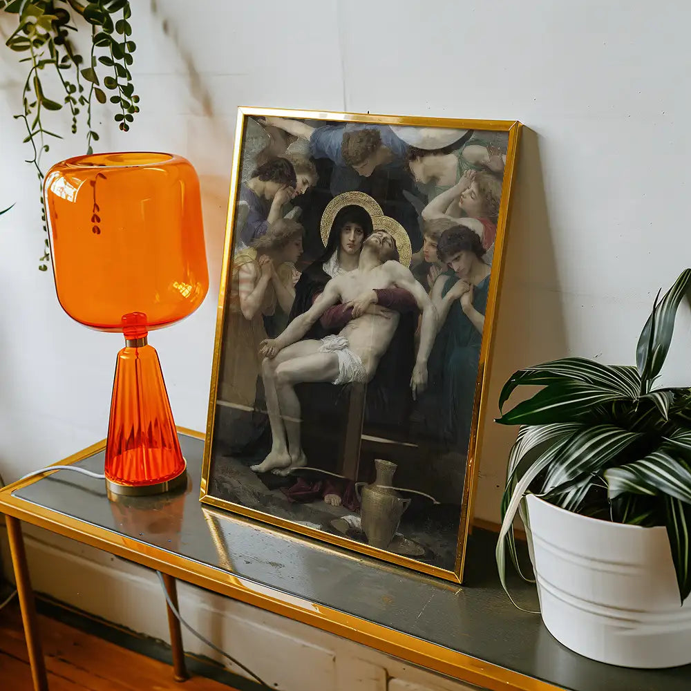 Framed painting of the Pietà, featuring Jesus and Mary surrounded by mourners, displayed on a stylish table beside an orange lamp and a potted plant.