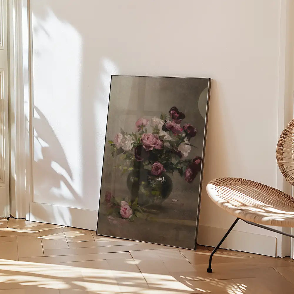 A framed painting of a floral arrangement featuring roses in a vase, leaning against a wall in a well-lit room with wooden flooring and a stylish chair.