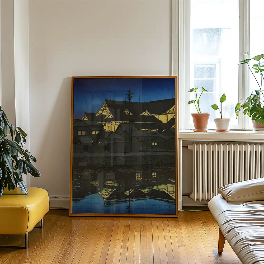 Framed painting of a night scene with illuminated buildings reflected in water, placed beside a potted plant and a yellow sofa in a bright room.