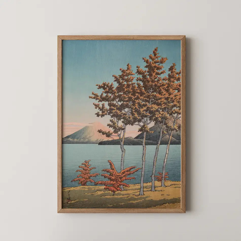 Framed painting of a serene landscape featuring trees and mountains near a lake, with autumn foliage in warm colors.
