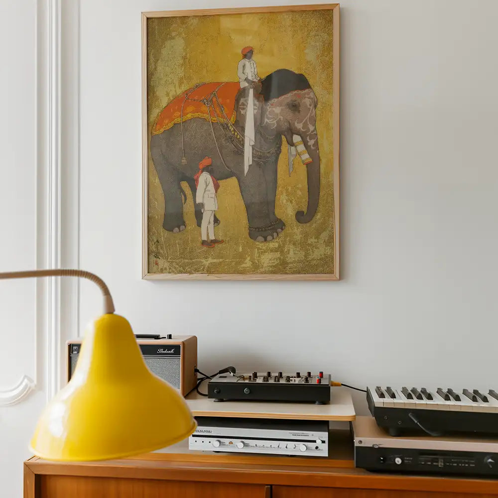 Framed painting of an elephant with a rider, displayed on a white wall above a wooden console with audio equipment and a yellow lamp.