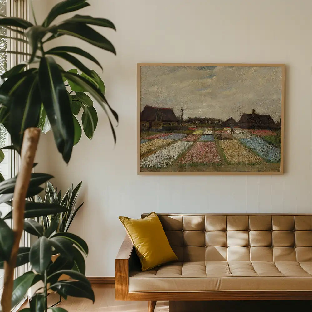Framed painting of a rural landscape with colorful flower fields and cottages, displayed on a wall above a cream-colored sofa with a yellow cushion.