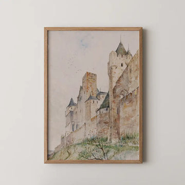 Framed watercolor painting of a medieval castle with turrets and walls, hung on a white wall.