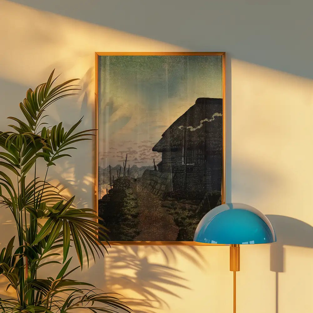 A vintage-style painting featuring a rustic house set against a serene landscape, framed in gold, displayed in a bright room with a plant and a modern lamp.