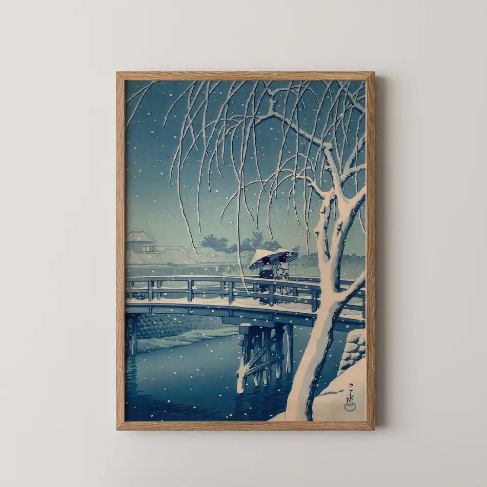 Framed painting of a snowy scene featuring a couple under an umbrella crossing a bridge, with traditional Japanese architecture in the background.