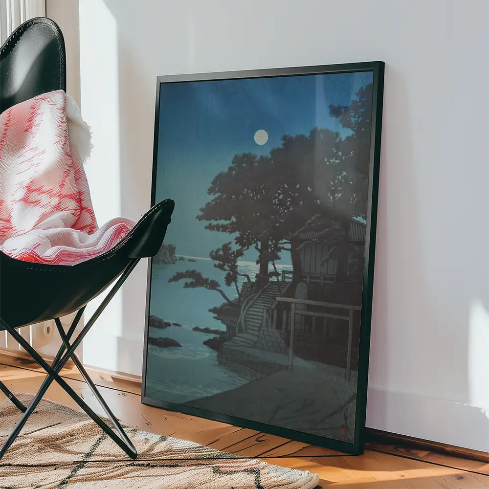 Framed painting of a serene landscape with a moonlit sky, leaning against a wall next to a black chair and a patterned rug.