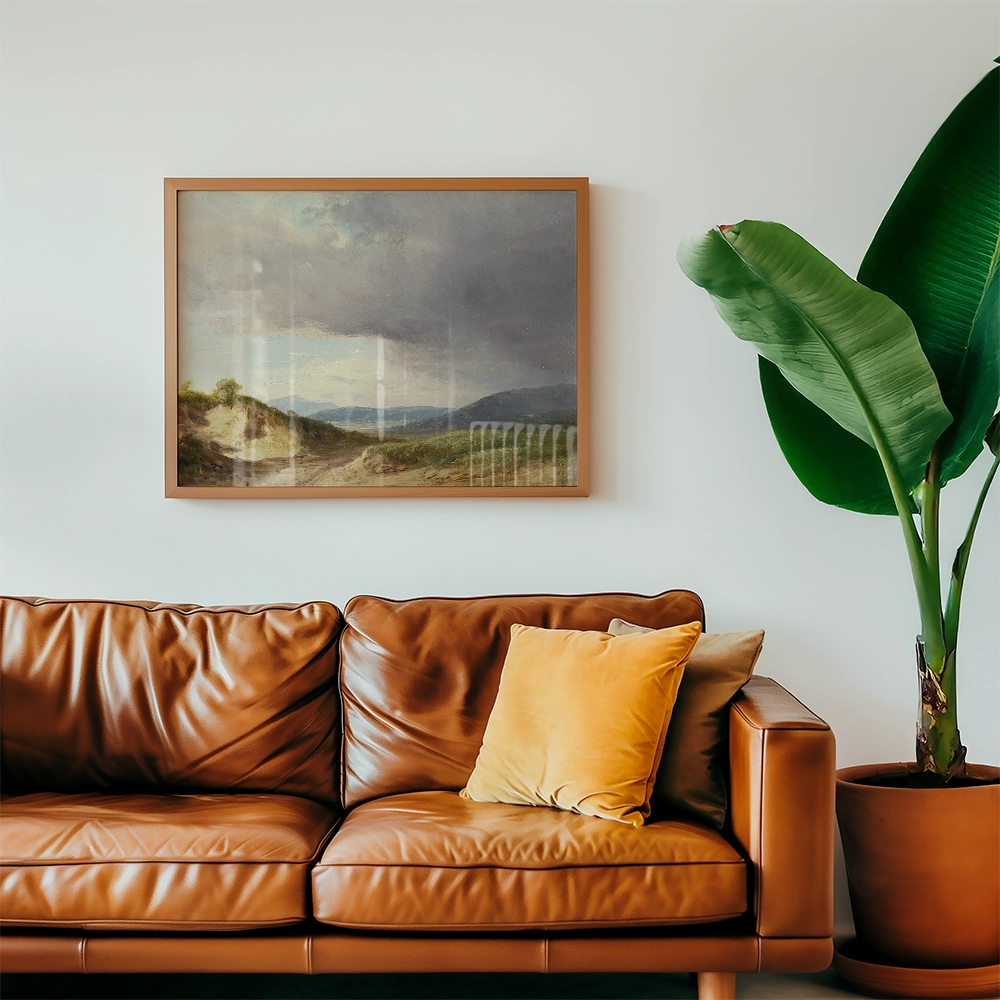 A framed landscape painting hanging on a wall above a brown leather sofa with a yellow cushion and a green plant nearby.