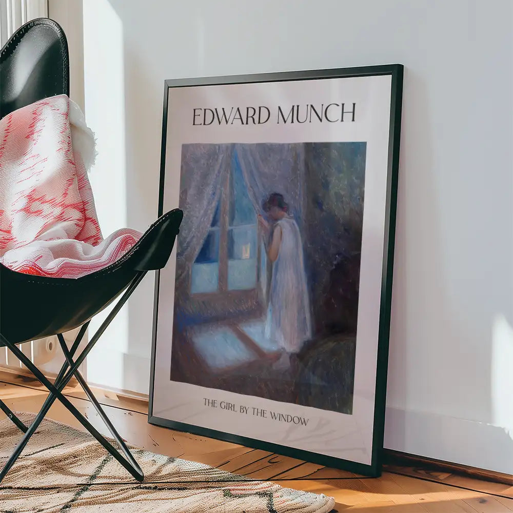 Framed poster of "The Girl by the Window" by Edward Munch, placed next to a black chair and a patterned blanket on a wooden floor.
