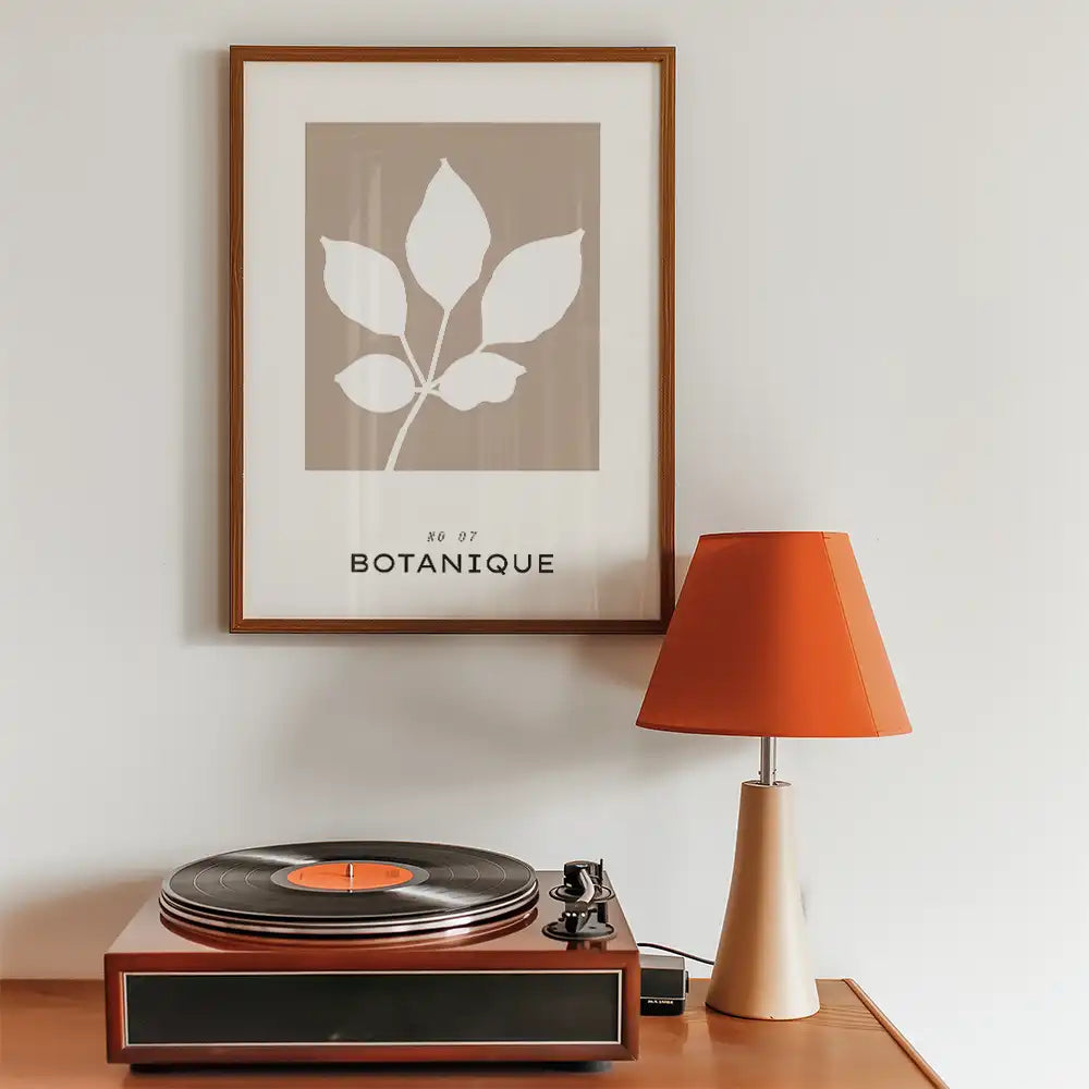 Modern botanical art print featuring a leaf design in neutral tones, framed and styled with a vintage record player and orange lamp.