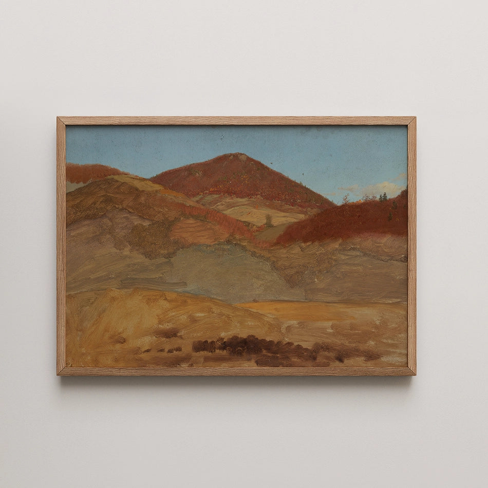 Landscape painting featuring rolling hills in warm tones with a blue sky, framed in light wood.