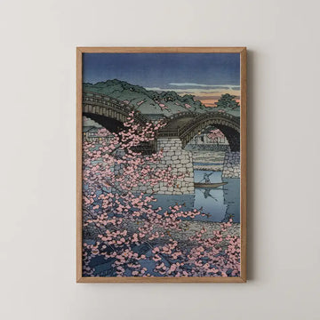 Framed painting of a serene landscape featuring a river, traditional bridges, cherry blossom trees, and a small boat at sunset.