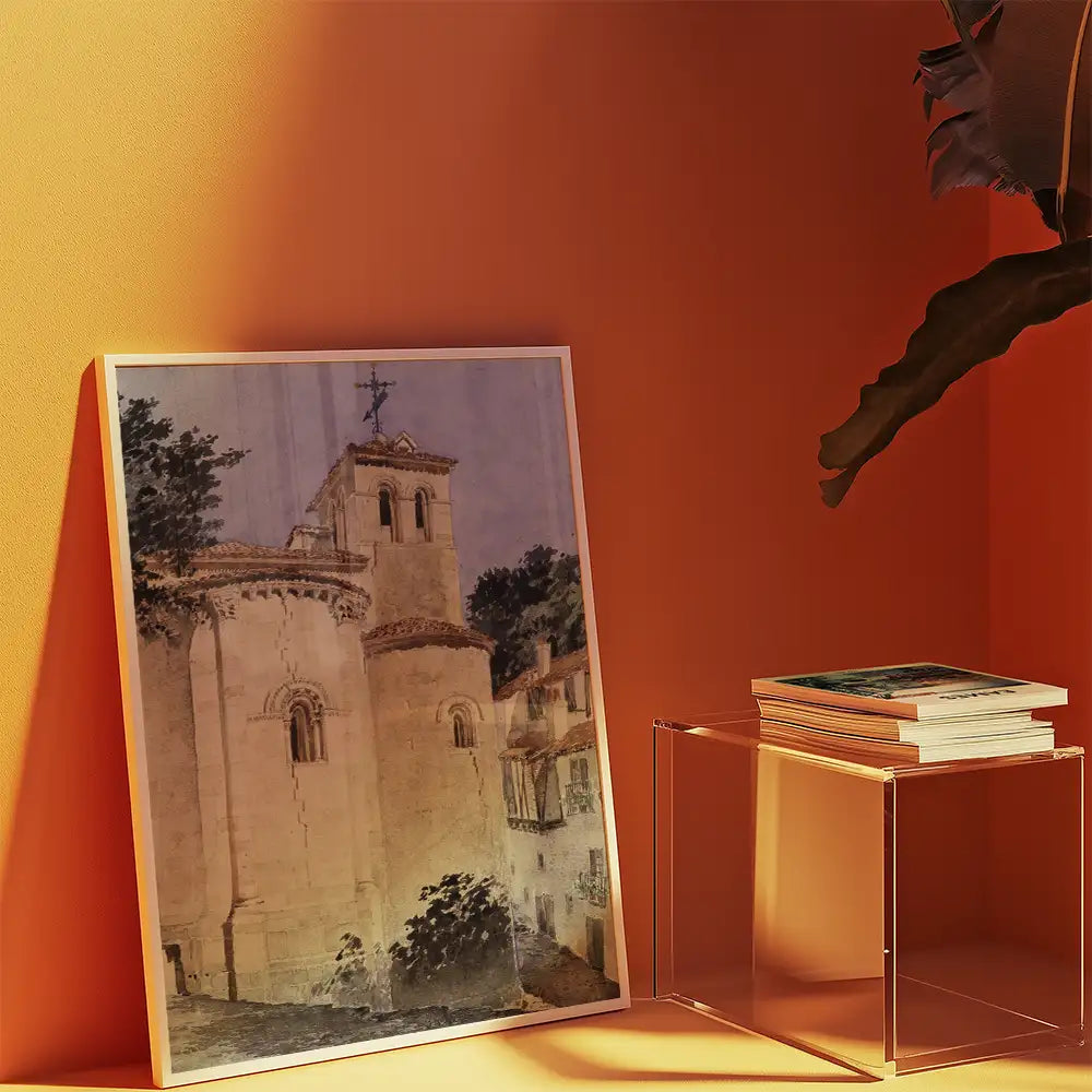 Painting of a church with a tower, framed and displayed against an orange wall, beside a clear acrylic table with stacked books.