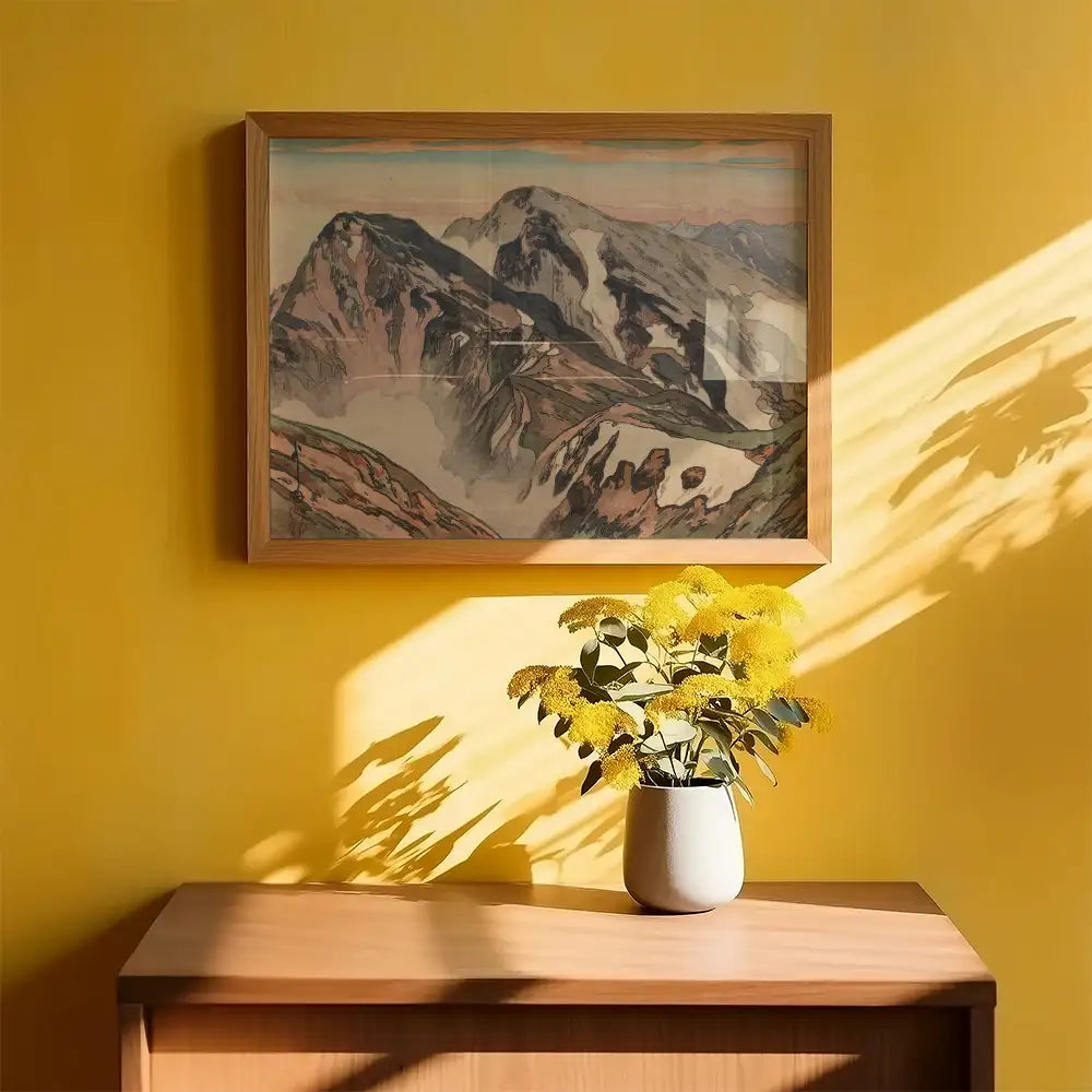 Framed mountain landscape painting on a vibrant yellow wall with a vase of yellow flowers on a wooden surface.