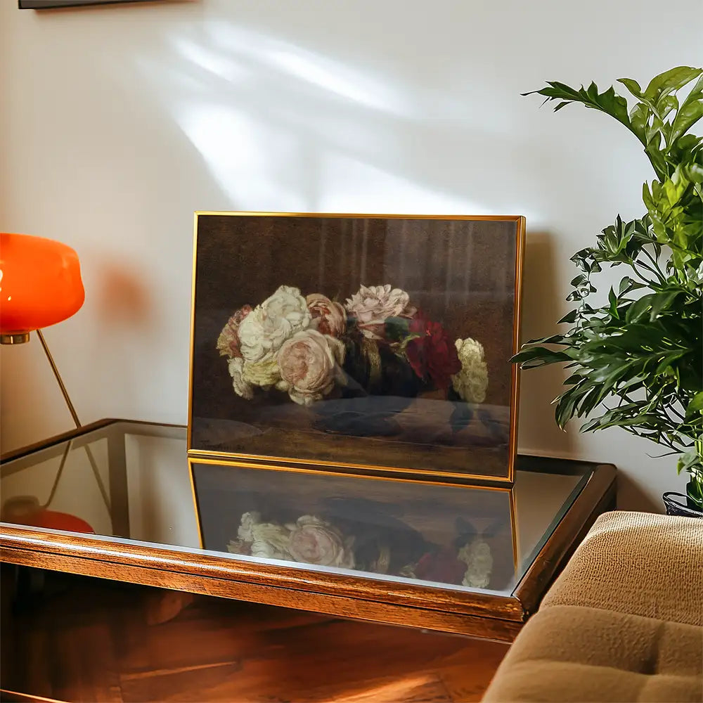 Framed painting of a bouquet of roses displayed on a wooden table next to a modern orange lamp and green plant.