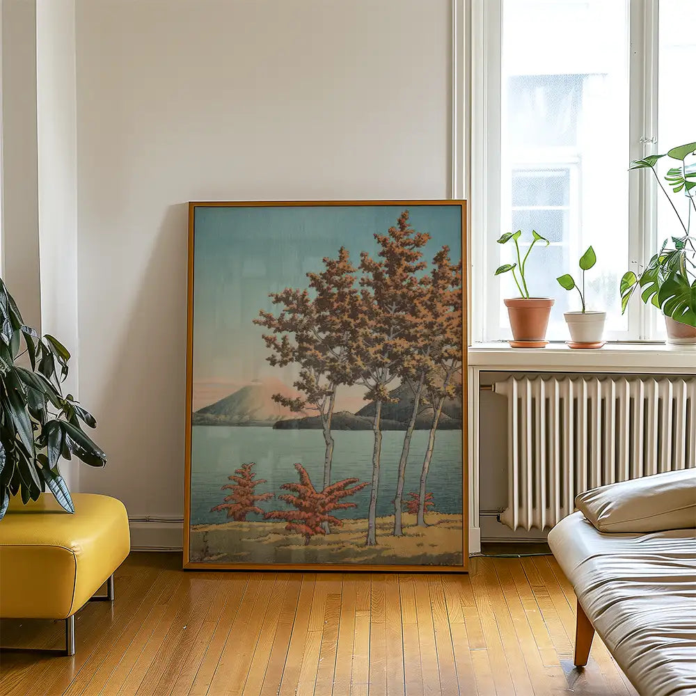 Framed painting of a serene landscape with trees and a lake, displayed in a bright, modern interior with plants and light wooden flooring.