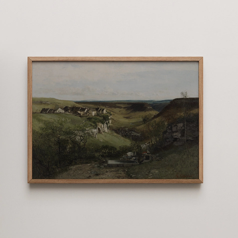Framed landscape painting showcasing a serene view of rolling hills and rocky cliffs with a distant village under a cloudy sky.