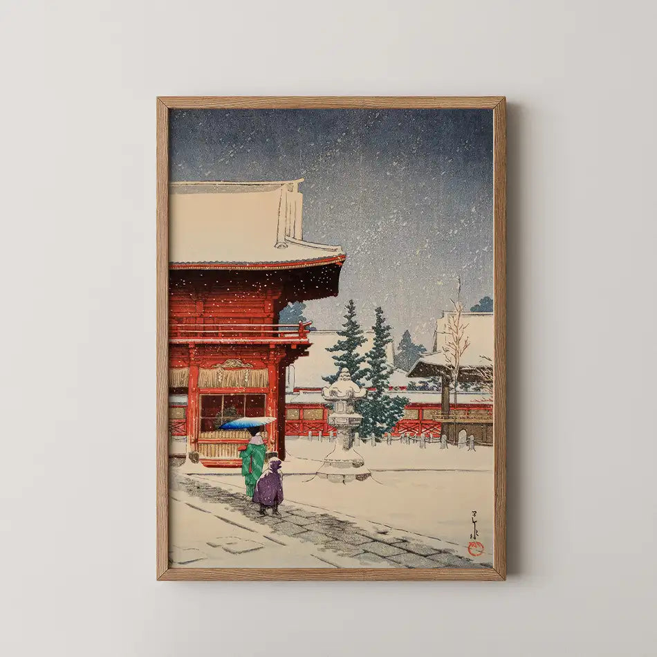 Framed painting of a traditional Japanese scene with two figures walking in the snow near a red temple and evergreen trees.
